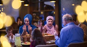 In a modern restaurant setting, a European Islamic family comes together for iftar during Ramadan, engaging in prayer before the meal, uniting tradition and contemporary practices in a celebration of photo
