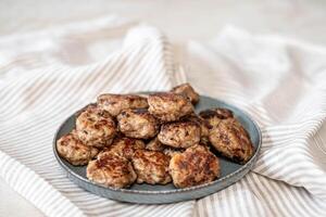 A rustic presentation of golden meatballs arrayed on a ceramic plate, against the soft lines of a crumpled striped napkin, ideal for a cozy dinner setting. photo