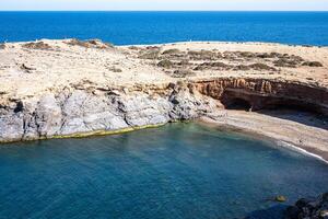A coastal inlet framed by rugged cliffs, a secluded beach inviting quiet moments under the bright blue sky, with sparse visitors. photo