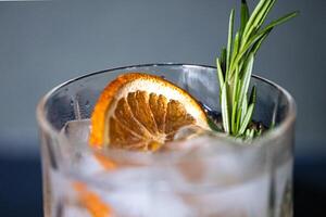 Glass of gin tonic cocktail with ice, sprig of rosemary and sliced dry orange photo