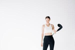 Beautiful and slender woman in a short sports top stands with a mat in her hands, on a white background, copy space photo