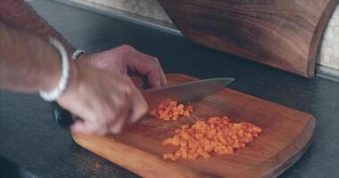 Home cooking. A man chops carrots on the kitchen table with a large knife on a wooden board video