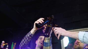 Handsome friends clinking bottles of beer and smiling while resting at the pub video