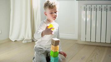 Little boy building tower of block toys sitting on floor in sunny bedroom. Child playing with colorful toy blocks. Kids play. Educational game for baby and toddler. Children build toy house video