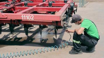 The engineer paints the elements of the housing of agricultural machinery. Painting the seeder's body elements in red. Preparation of equipment for winter video