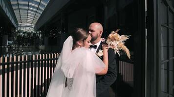 Bride and Groom Embracing in Elegant Wedding Venue. The bride, dressed in a beautiful white gown with a flowing veil, holds a bouquet of dried flowers while the groom, in a black tuxedo, gently video
