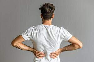 Man with back pain standing against a gray wall photo