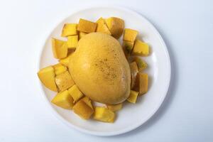 Ripe mango with sliced mango around it on white plate isolated on white background. photo