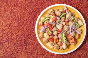 Ready to cook healthy food meal maker curry. Potatoes, onions, tomatoes, green chillies on yellow plate. photo