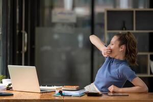 businesswoman yawning and stretching lazy while working with a laptop computer. Feeling bored and tired photo