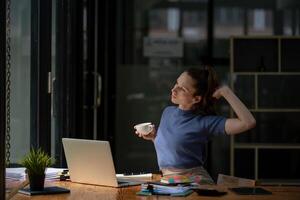 Businesswoman stretching lazy at the desk to relax while take a break from work and enjoy with coffee in the office. Feeling stressed and achy from work. photo