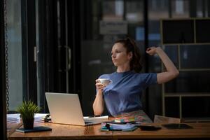 Businesswoman stretching lazy at the desk to relax while take a break from work and enjoy with coffee in the office. Feeling stressed and achy from work. photo