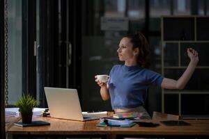 Businesswoman stretching lazy at the desk to relax while take a break from work and enjoy with coffee in the office. Feeling stressed and achy from work. photo