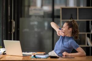 businesswoman yawning and stretching lazy while working with a laptop computer. Feeling bored and tired photo