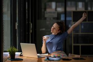 Businesswoman stretching lazy at the desk to relax while take a break from work and enjoy with coffee in the office. Feeling stressed and achy from work. photo
