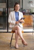 Portrait of a smart businesswoman sitting cross-legged on a chair and holding a digital tablet. photo