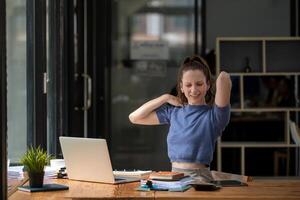 Businesswoman stretching lazy at the desk to relax while working in the office. Feeling stressed and achy from work. photo