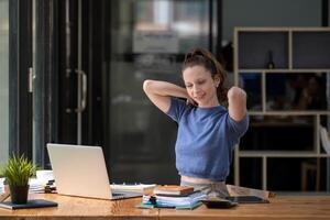 Businesswoman stretching lazy at the desk to relax while working in the office. Feeling stressed and achy from work. photo