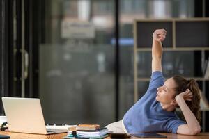 Businesswoman stretching lazy at the desk to relax while working in the office. Feeling stressed and achy from work. photo
