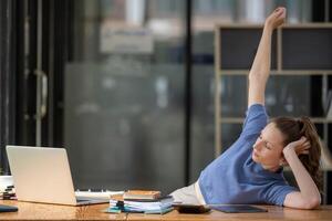 Businesswoman stretching lazy at the desk to relax while working in the office. Feeling stressed and achy from work. photo