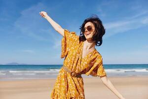 Woman in yellow dress standing on beach with arms outstretched enjoying the beauty of nature on photo