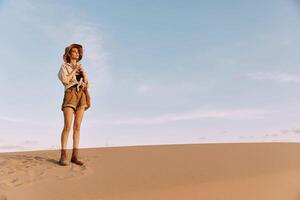 Woman standing on top of sand dune with hands in pockets, enjoying peaceful desert view photo