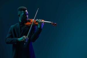 Talented young African American man playing violin on dark blue background with copy space photo