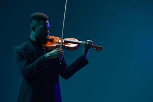 Talented young African American man playing violin gracefully in front of a dark blue background photo