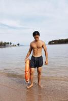 The Alert Lifeguard. A Joyful Asian Man Guarding the Beach, Rescuing Swimmers with a Lifebuoy in the photo