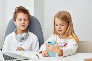 Happy children studying at home using laptops and tablets for elearning, sitting at a table in their photo
