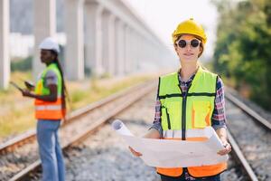 Portrait engineer women on railway tracks construction site with blueprint roll working project manager in suburb transportation line photo