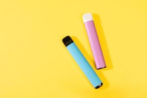disposable electronic cigarettes with shadow on a yellow background with copy space. The concept of modern smoking, vaping and nicotine. top view. photo