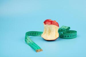 Red bitten apple and measuring tape on a blue background with copy space. photo