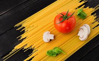 Spaghetti with tomato, mushrooms and spinach on black background. Top view. Healthy eating concept. Preparation of products. photo