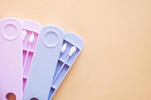 Reusable silicone ear sticks in colored cases with a top view on a beige background. An alternative to disposable cotton swabs. Reduce costs and save money. photo