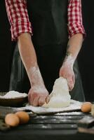 Beautiful and strong men's hands knead the dough from which they will then make bread, pasta or pizza. A cloud of flour flies around like dust. Next to the chicken egg. The background is dark. photo