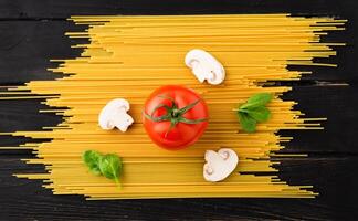 Spaghetti with tomato, mushrooms and spinach on black background. Top view. Healthy eating concept. Preparation of products. photo