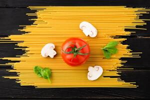 Spaghetti with tomato, mushrooms and spinach on black background. Top view. Healthy eating concept. Preparation of products. photo