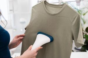 Using steaming iron to ironing t-shirt in home. Doing stream vapor iron for press clothes in hand. photo