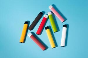 Layout of colorful disposable electronic cigarettes with shadows on a blue background. The concept of modern smoking, vaping and nicotine. Top view photo
