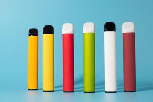 Set of colorful disposable electronic cigarettes with shadows on a blue background. The concept of modern smoking, vaping and nicotine. Top view photo
