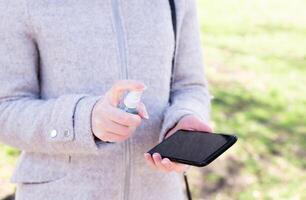 Close up female hand holding smartphone and cleaning spray on her smartphone. Good personal hygiene practices on the street photo