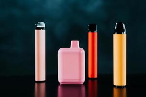 A set of colorful disposable electronic cigarettes of different shapes on a black background with smoke. Concept of modern smoking, vaping and nicotine. photo