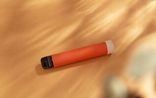orange stick - disposable vaping device, electronic cigarette on a beige background. Flat lay, top view, minimal design with shadows of sunlight. photo