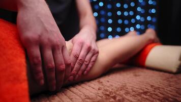 Shallow depth of field close-up of male hands massaging the ankle of a young woman in a professional massage room video