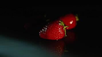 Juicy bright fresh strawberries lie on a black background in the dark. video