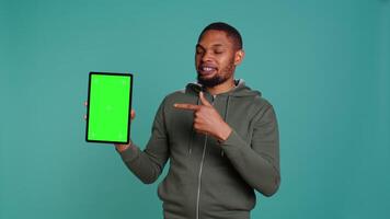 Joyous african american man holding isolated screen laptop, doing recommendation. Upbeat person pointing towards chroma key device, giving positive feedback, studio background, camera B video