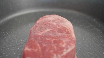 Raw meat. Action.A large black frying pan that heats up to start frying a beautiful large steak. video