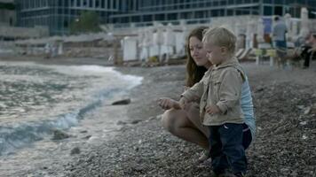 Mom and child throw stones into sea. Creative. Mother and child are relaxing at sea and playing on beach with stones. Mother and child are resting on shore throwing stones video