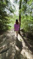 A young woman in a pink shirt and shorts walking through a forest path towards a serene lake, with sunlight filtering through the trees, capturing the essence of outdoor adventure and nature's tranquility video